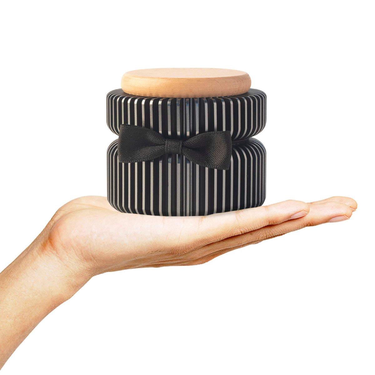 Dark gray keepsake urn held in palm for size reference – black vertical striped aluminum, black bow tie, beech wood lid, compact and portable