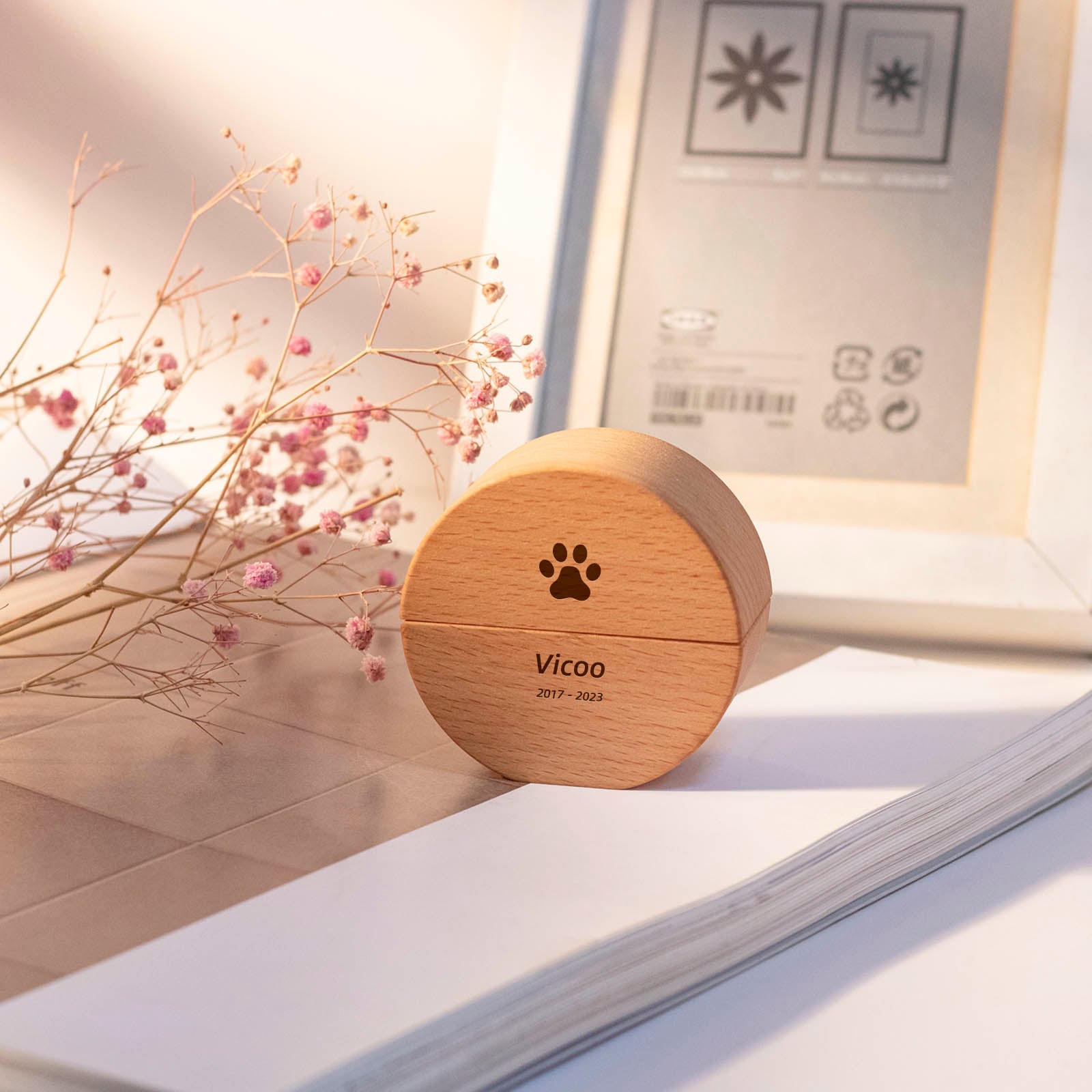 Pet memorial round wooden keepsake urn – engraved paw print with name "Vicoo" and dates 2017-2023, on desk with dried flowers and photo frame