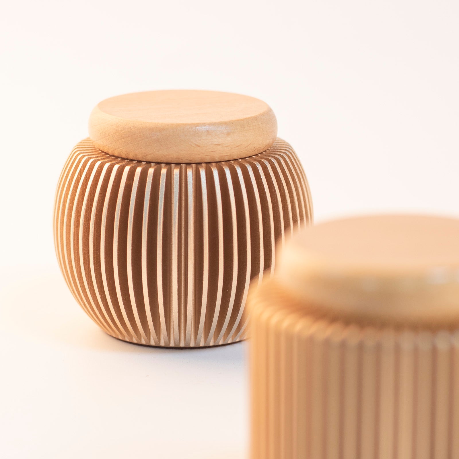 Rose gold keepsake urn close-up – vertical stripe texture on anodized aluminum shell with natural beech wood lid