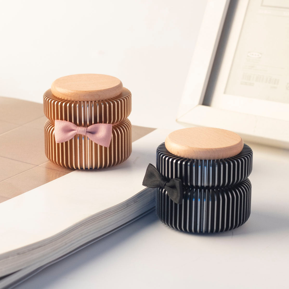 Rose gold and dark gray keepsake urns displayed side by side on book – two color options for family sharing, anodized aluminum with beech wood lids and ribbon bows