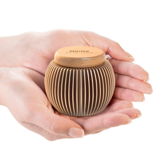 Custom engraved keepsake urn held in hands – egg-shaped aluminum & beech wood